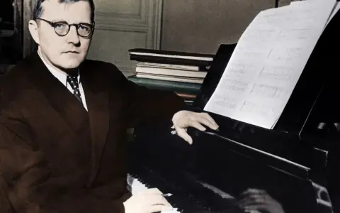 Dmitri Szostakowicz w okularach siedzi przy fortepianie, grając z nut.