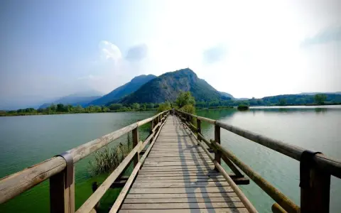 Ponte in legno su lago calmo, montagne verdi sullo sfondo. Un luogo incantevole per scoprire cosa vedere in Franciacorta, tra natura e tranquillità.