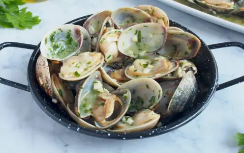 Almejas en salsa verde, un plato delicioso con mariscos frescos y perejil picado, listo para disfrutar.