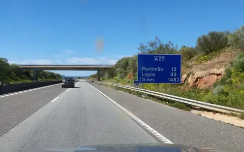 Autobahn A22 in Portugal. Ein Auto fährt auf der rechten Spur, vorbei an einem Schild mit Zielen wie Portimão und Lagos.