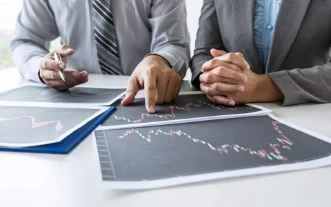 Dwóch biznesmenów analizuje wykresy, omawiając strategię finansową, być może dotyczącą kredytu pomostowego.