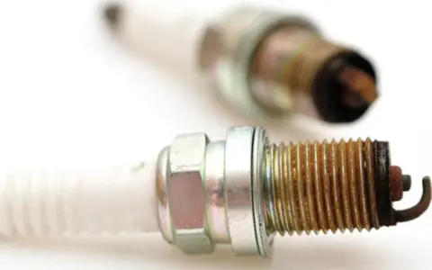 Two used spark plugs for cars, showing wear and tear on their metal tips.