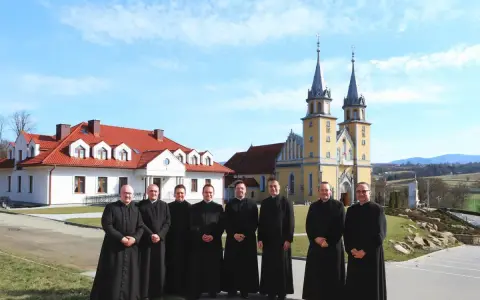 Grupa księży w czarnych szatach przed żółtym kościołem. Czy to miejsce, gdzie zbierany jest podatek na kościół?