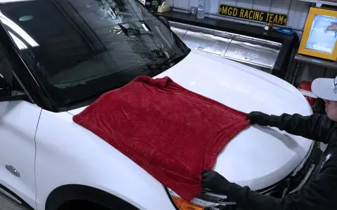 Person in gloves carefully places a plush red towel on a white car hood, demonstrating the best way to wash a car without scratching.