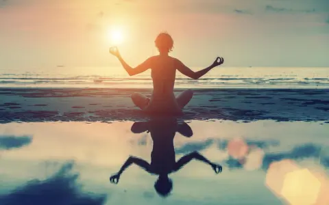 Frau in Lotusposition am Strand bei Sonnenuntergang. Ihre Meditation stärkt das Selbstbewusstsein.