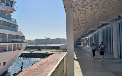 Una nave da crociera attracca nel porto di Leixões, Portogallo. Due persone passeggiano sotto una moderna tettoia con un soffitto decorato.
