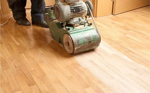Ein Handwerker bearbeitet mit einer Schleifmaschine einen Holzboden. Das Parkett wird abgeschliffen, um ihm neues Leben einzuhauchen.