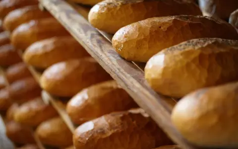 Rzędy czerstwego chleba na drewnianych półkach. Niektóre bochenki posypane są makiem.