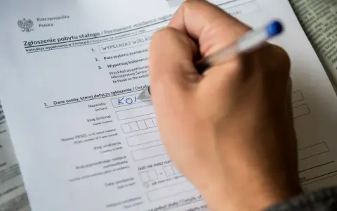 Ręka wypełnia formularz "Zgłoszenie pobytu stałego". Czy jest obowiązek meldunku? Tak, ten dokument to potwierdza.