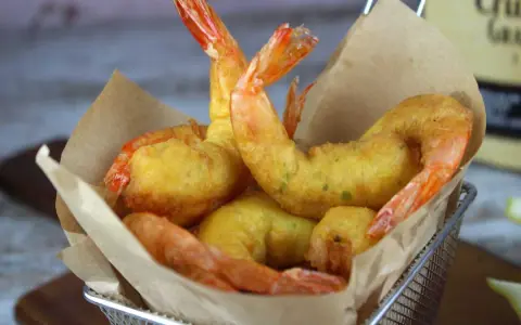Crujientes gambas a la gabardina doradas y sabrosas, servidas en una cesta metálica con papel de cocina.