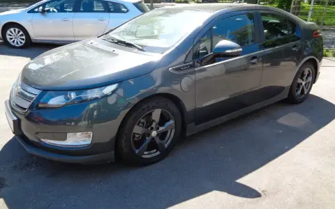 Ciemnoszary Chevrolet Volt stoi na parkingu. Obok niego widać srebrne kombi.
