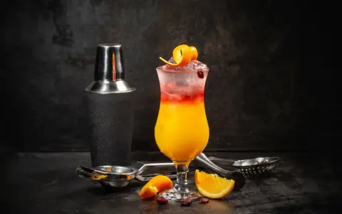 Kolorowy drink Sex on the Beach z pomarańczą i żurawiną, obok shakera i akcesoriów barmańskich. Idealny przepis na lato!