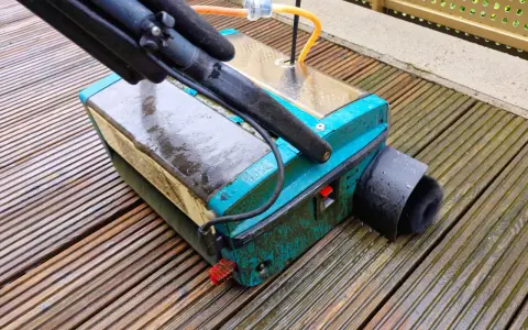 Gerät zur Bankirai Terrasse reinigen mit Bürstenaufsatz auf nassen Holzbrettern.