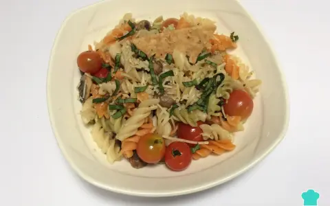 Pasta tricolor con tomates cherry, albahaca y queso rallado en un plato blanco.