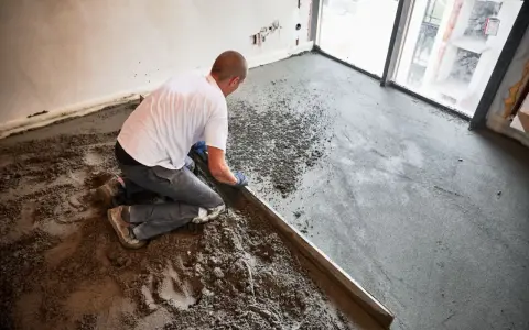 Budowlaniec wyrównuje świeży, suchy beton na posadzkę za pomocą łaty.