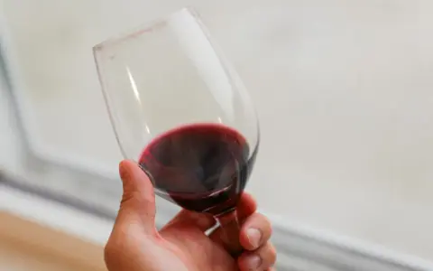 Dłoń trzyma kieliszek czerwonego wina. Czy wino jest zdrowe? To pytanie nurtuje wielu miłośników tego trunku.