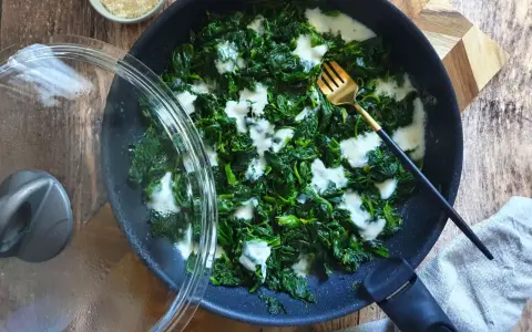 Spinaci in padella cremosi, con una forchetta dorata pronta ad assaggiarli. Un contorno semplice e gustoso.