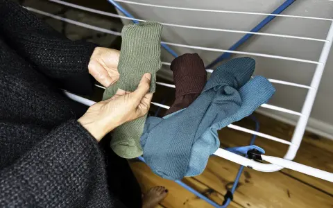 Hände sortieren frisch gewaschene, bunte Socken auf einem Wäscheständer.