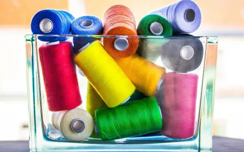 Un assortiment coloré de bobines de fil coton ou polyester, empilées dans un pot en verre.
