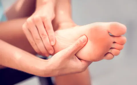 Hands massaging a foot, seeking aching feet remedy. The sole of the foot shows a slight red hue, indicating discomfort.