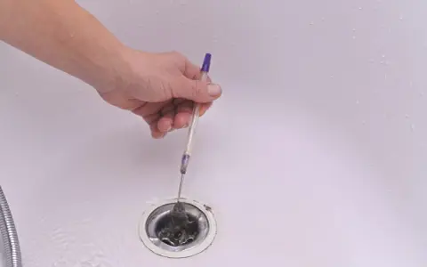 Mano retirando pelos y suciedad del desague plano de una bañera con un bolígrafo.