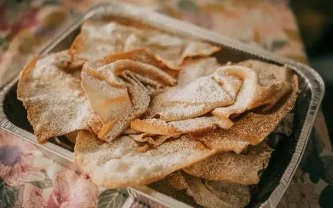 Orejas de carnaval espolvoreadas con azúcar glas en una bandeja metálica. ¡Perfectas para tu receta!