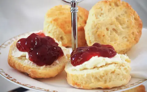 Was sind Scones? Köstliche, goldbraune Scones, bestrichen mit Clotted Cream und Marmelade, auf einer Etagere serviert. Ein Genuss für jeden Teeliebhaber.