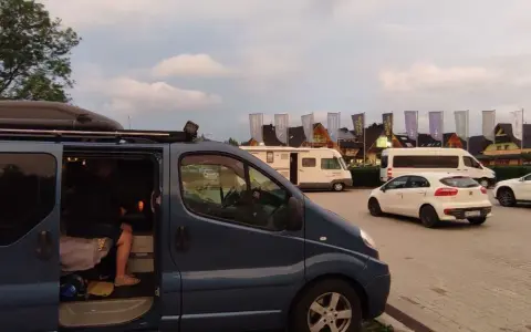 Na parkingu przy Chochołowskich Termach stoi ciemnoniebieski bus, biały samochód i kamper.
