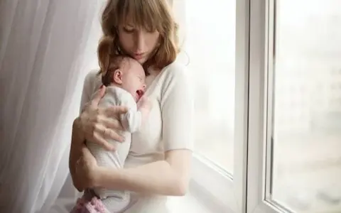 Zmęczona mama tuli płaczące dziecko, które właśnie robi kupę w nocy.