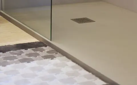 Plato de ducha de resina con desagüe cuadrado. Alfombra a cuadros en primer plano.