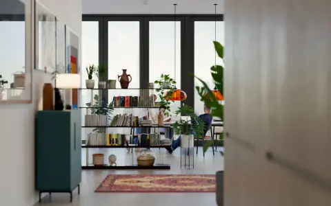 Un salón comedor dos ambientes con estanterías llenas de libros y plantas, y dos personas trabajando en una mesa.