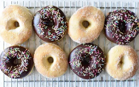 Åtta hemgjorda donuts, vissa med chokladglasyr och strössel, andra med socker. Perfekt för ett donuts recept!
