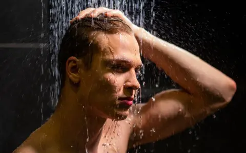 Ein Mann unter der Dusche, der sich die Haare wäscht. Die kalte Dusche ist eine Herausforderung, aber er hält durch.