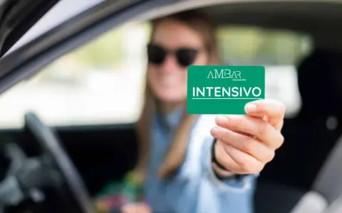 Mujer con gafas de sol muestra tarjeta "INTENSIVO" de autoescuela. Obtener el carnet B+E es difícil, pero este curso intensivo puede ayudar.