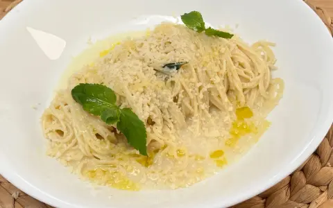 Spaghetti al limone cremosi, conditi con parmigiano e guarniti con foglie di menta fresca.