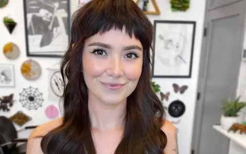 Uśmiechnięta kobieta z ciemnymi włosami i grzywką baby bangs.