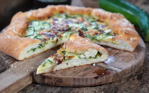 Leckeres Zucchini Pizza Rezept auf einem Holzbrett, mit einem Stück abgetrennt.