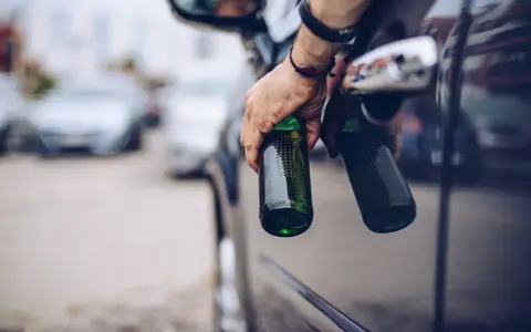 Mann hält zwei Bierflaschen aus dem Autofenster. Er versucht, den Alkohol abzubauen, indem er sie wegwirft.