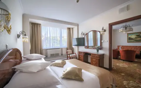 Elegancki pokój hotelowy z dużym łóżkiem, toaletką i widokiem na salon. Dowiedz się, ile kosztuje noc w hotelu Gołębiewski.