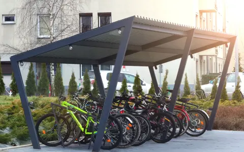 Zadaszona rowerownia w bloku, pełna rowerów gotowych do jazdy.