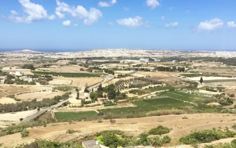 Malta, krajobraz jak z "Gry o tron", z polami uprawnymi, gajami oliwnymi i miastem w oddali.