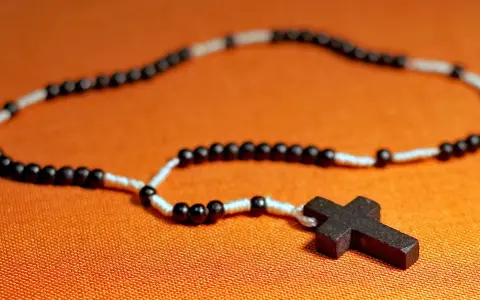 Różaniec z czarnymi i białymi paciorkami i drewnianym krzyżem. Symbolizuje modlitwę do anioła stróża.