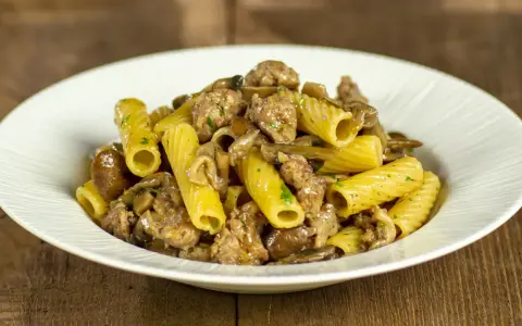 Piatto di pasta funghi e salsiccia, con rigatoni conditi con funghi trifolati e pezzetti di salsiccia saporita.