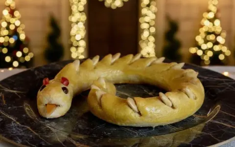 Dolci tipici Perugia: un serpente di pasta frolla dorata, con occhi rossi e lingua arancione, adagiato su un piatto scuro.
