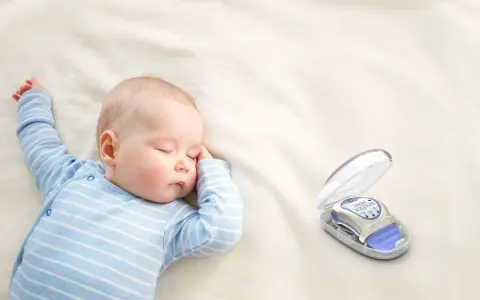 Śpiące dziecko w niebieskim pajacyku obok otwartego etui z monitorem oddechu dla niemowląt.