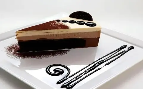 Deliciosa tarta de tres chocolates, con capas de mousse de chocolate blanco, con leche y negro, decorada con cacao y un toque de galleta.