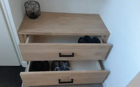 Meuble à chaussures fait maison en bois clair, avec deux tiroirs ouverts contenant des bottes et des baskets.