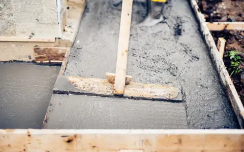 Prace budowlane: świeży beton bez żwiru, starannie wylany w drewnianej formie. Drewniana łopata wyrównuje powierzchnię.
