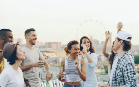 Groupe d'amis souriants et dansant sur un toit, avec une grande roue en arrière-plan.