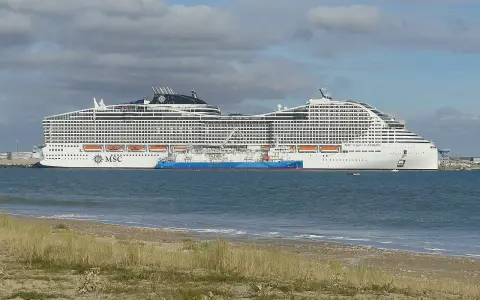 A large white MSC World Europa cruise ship docked next to a blue tanker ship in the sea.